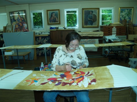 A woman brushing colours onto a cloth with a bright bird and flower design at a dyeing workshop