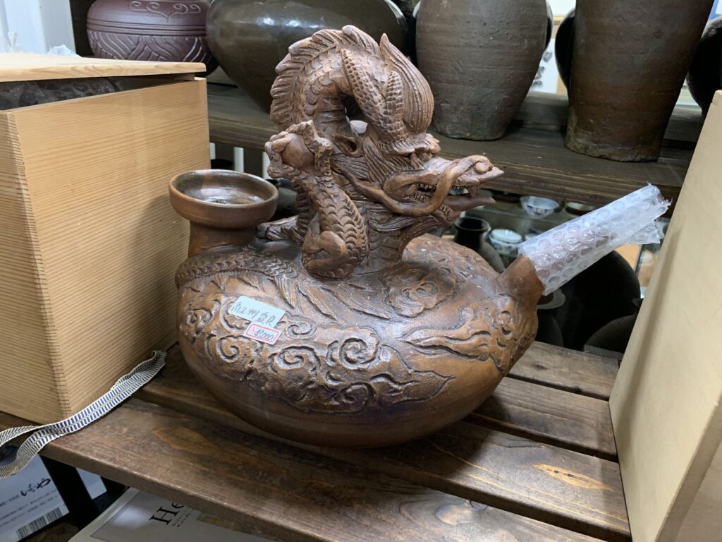 A ceramic pot shaped and decorated with a coiled dragon on a shelf in a pottery shop in Naha