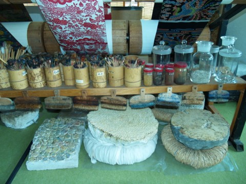 Shelves of pigment jars and brush pots above rolled materials at a dyeing workshop