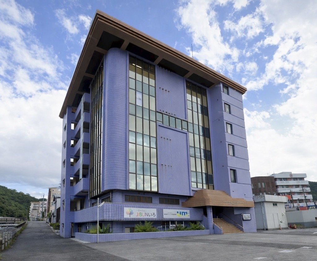 A six-storey purple building with tall windows and a brown entrance canopy under a blue sky
