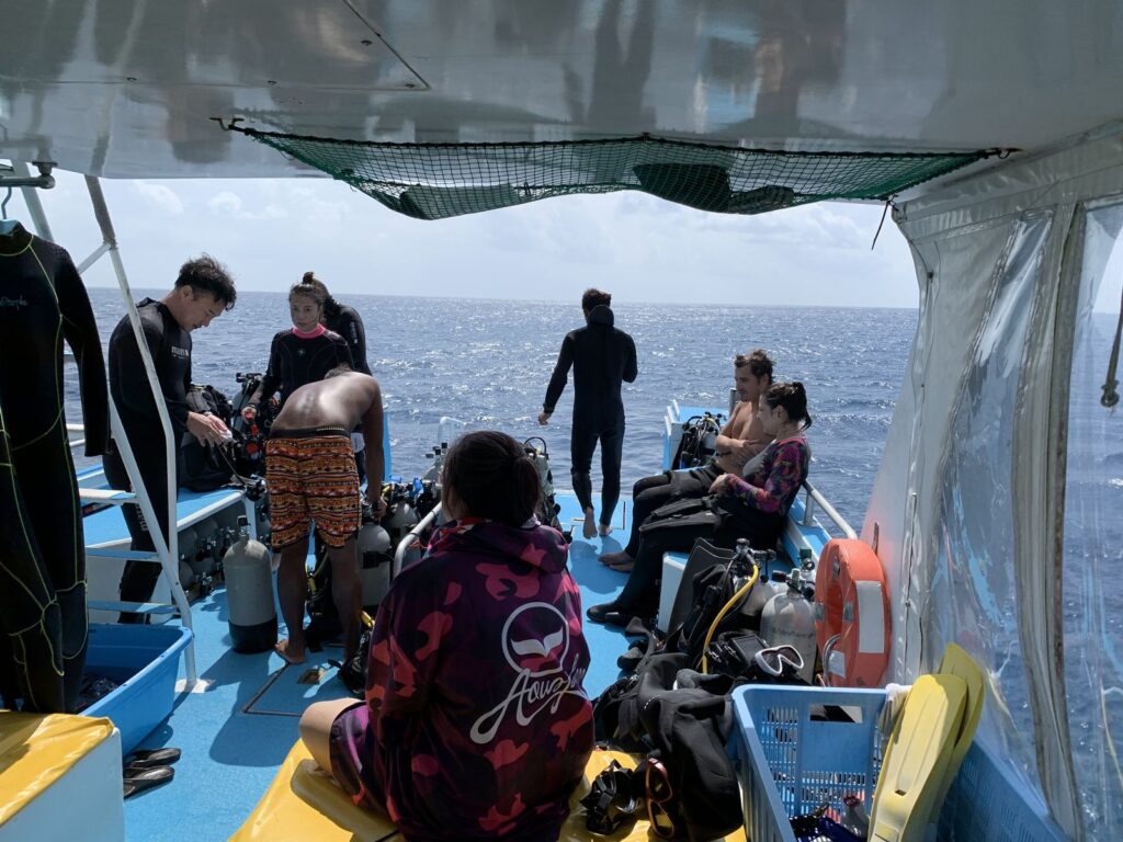 Divers in wetsuits with tanks and gear on the deck of a dive boat at sea off Ishigaki