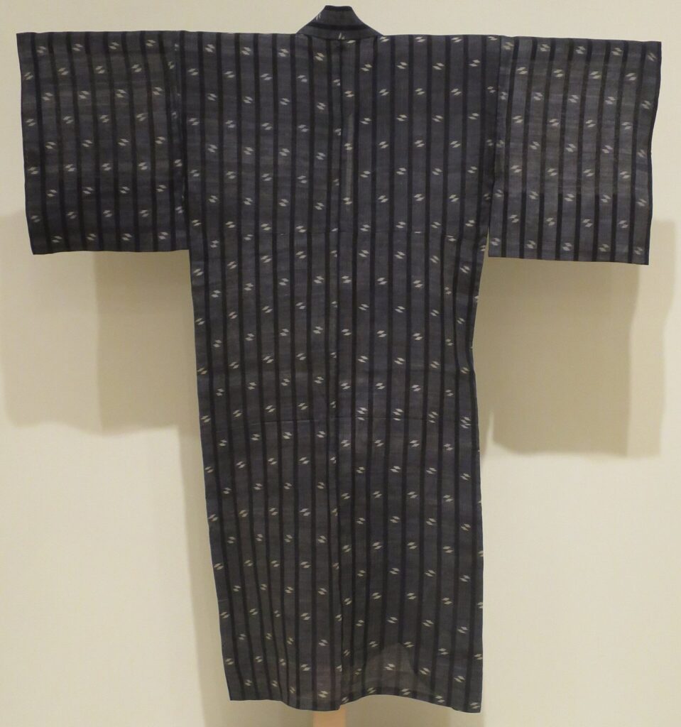 Dark blue-grey kimono hung on a wall, with rows of small white kasuri marks and fine vertical stripes