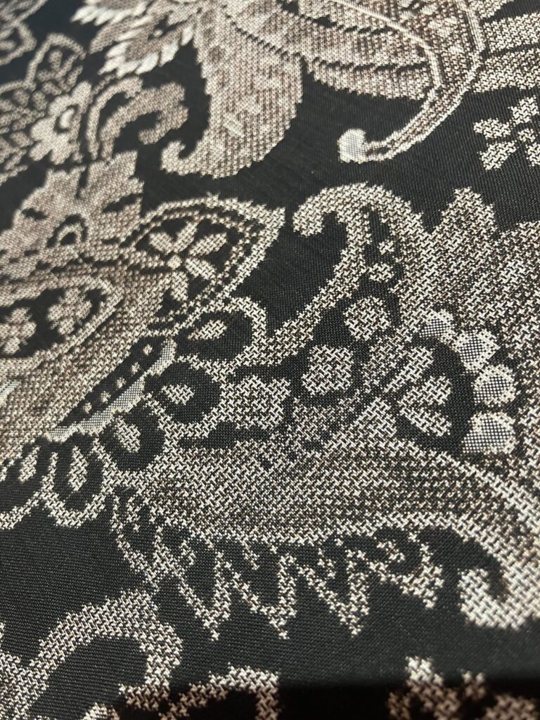 Close-up of black silk cloth with a fine pale grey paisley-like pattern made of tiny kasuri dots
