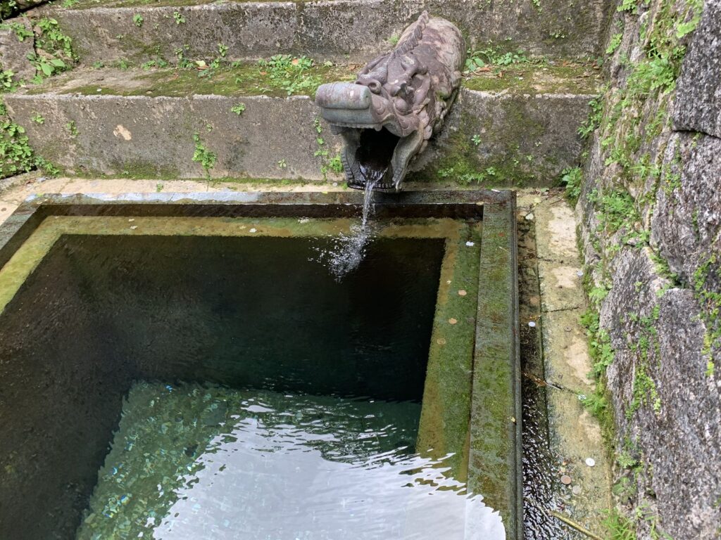 Water pouring from a carved stone dragon-head spout into a stone basin at Shuri Castle
