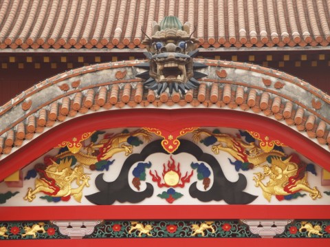 Close-up of a carved dragon head and gold dragon decoration above the entrance of a red hall at Shuri Castle