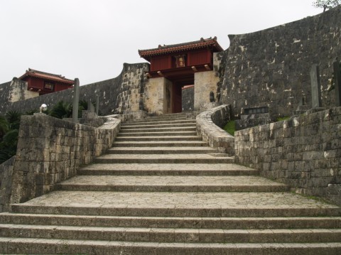 Stone stairway leading up between castle walls to a red gate at Shuri Castle