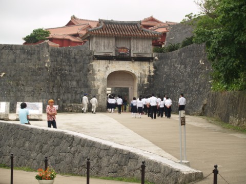 Curved stone walls and an arched stone gate topped by a red-roofed wooden tower at Shuri Castle