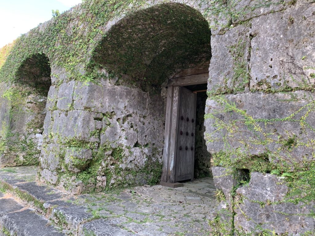 Arched stone gates with wooden doors in a moss-covered limestone wall at the Sogenji ruins, Naha