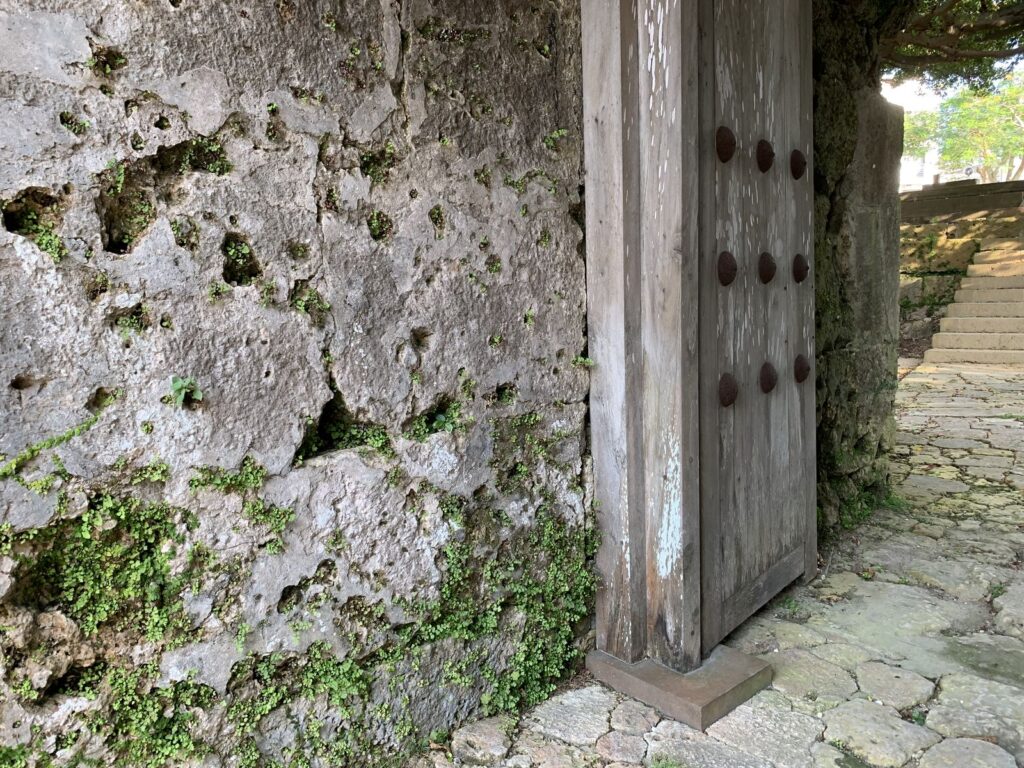A wooden door set in a thick, weathered limestone wall beside a stone-paved path at the Sogenji ruins, Naha