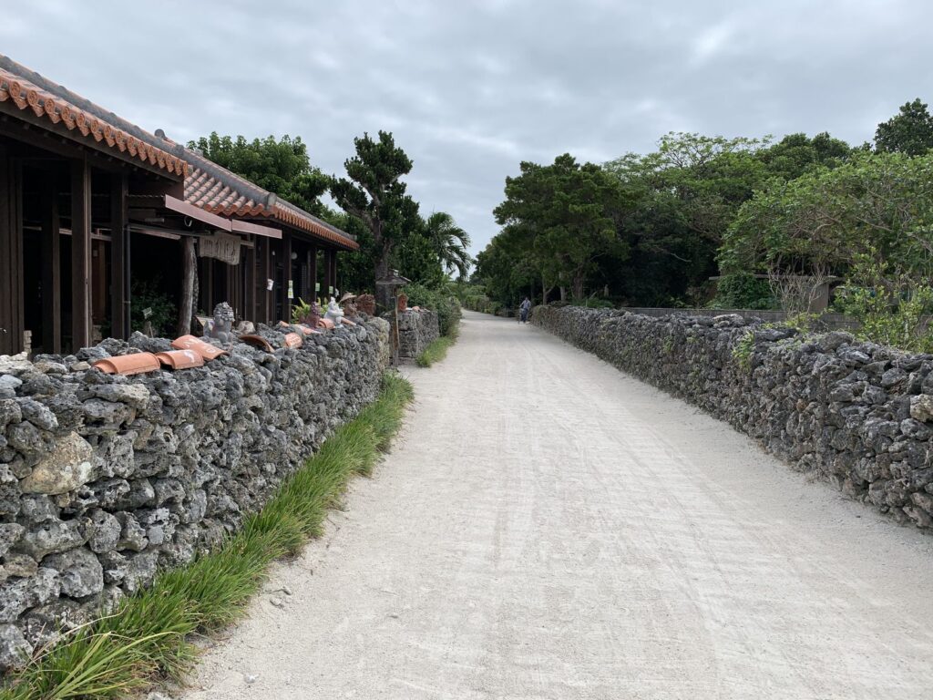 A white sand lane lined by coral-stone walls with red-tiled roofs and trees, Taketomi