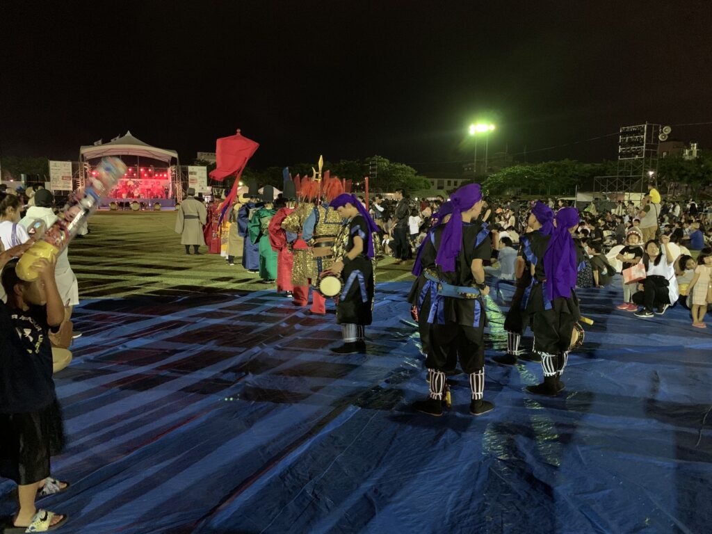 Performers with drums and banners in a night parade before a crowd at the Urasoe Tedako Festival