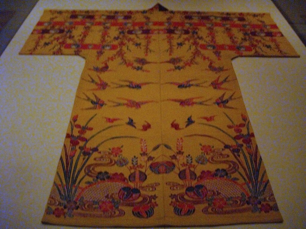 Yellow robe laid flat, dyed with birds, hanging branches, irises and flowing water above round bundles